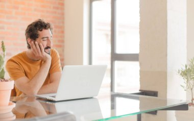 Evde dizüstü bilgisayarla çalışan sakallı genç bir adam.