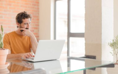 Evde dizüstü bilgisayarla çalışan sakallı genç bir adam.