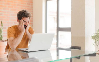 Evde dizüstü bilgisayarla çalışan sakallı genç bir adam.