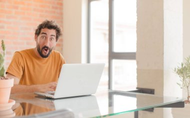 Evde dizüstü bilgisayarla çalışan sakallı genç bir adam.