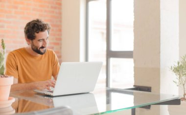 Evde dizüstü bilgisayarla çalışan sakallı genç bir adam.