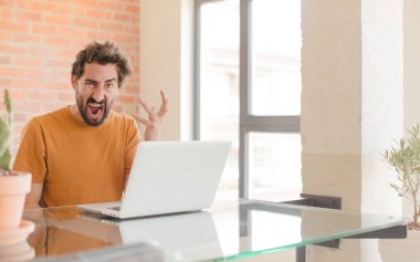 Evde dizüstü bilgisayarla çalışan sakallı genç bir adam.