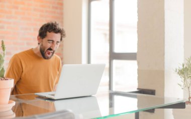 Evde dizüstü bilgisayarla çalışan sakallı genç bir adam.