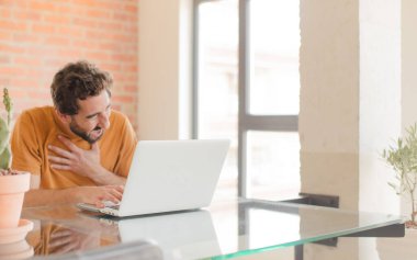 Evde dizüstü bilgisayarla çalışan sakallı genç bir adam.