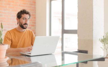 Evde dizüstü bilgisayarla çalışan sakallı genç bir adam.