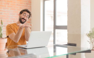 Genç sakallı adam gülerek güler yüzlü, kendine güvenen, olumlu bakışlı, bir nesne ya da konsept sunan ve bir dizüstü bilgisayarla çalışan