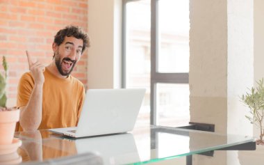 Genç sakallı adam bir fikri fark ettikten sonra mutlu ve heyecanlı bir dahi gibi hissediyor, neşeli bir şekilde parmağını kaldırıyor, eureka! Ve bir dizüstü bilgisayarla çalışmak.