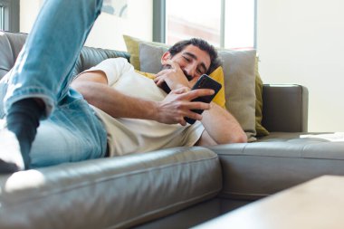 Genç sakallı adam akıllı telefonuyla kanepede dinleniyor.