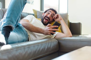 Genç sakallı adam akıllı telefonuyla kanepede dinleniyor.