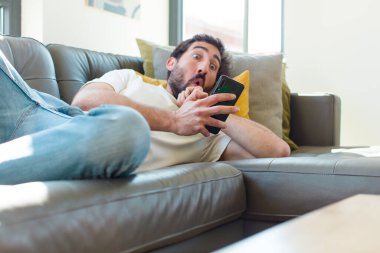 Genç sakallı adam akıllı telefonuyla kanepede dinleniyor.