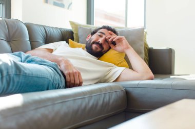 Genç sakallı adam kanepede dinleniyor.