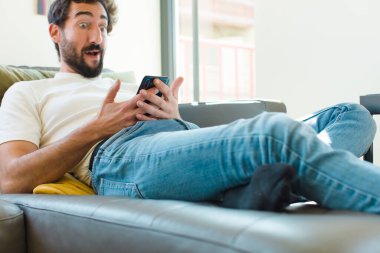 Genç sakallı adam akıllı bir telefonla kanepede dinleniyor.