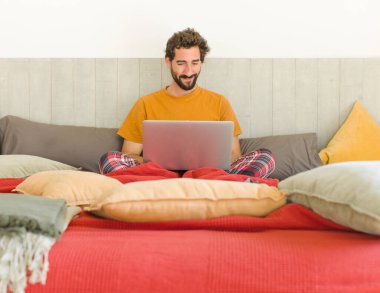 Yatakta dizüstü bilgisayarlı genç sakallı bir adam.