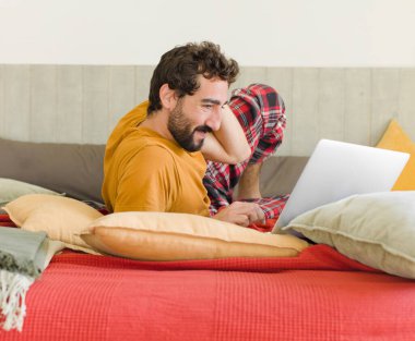 Yatakta dizüstü bilgisayarlı genç sakallı bir adam.