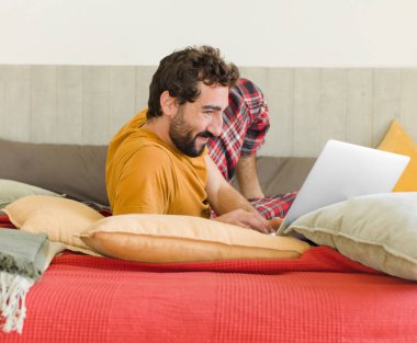 Yatakta dizüstü bilgisayarlı genç sakallı bir adam.