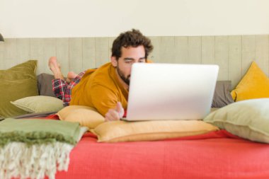 Yatakta dizüstü bilgisayarlı genç sakallı bir adam.
