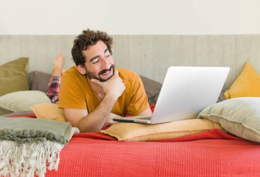 Yatakta dizüstü bilgisayarlı genç sakallı bir adam.