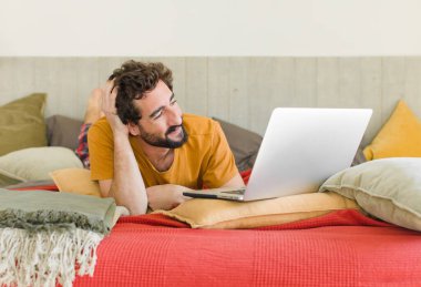 Yatakta dizüstü bilgisayarlı genç sakallı bir adam.