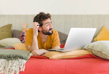 Yatakta dizüstü bilgisayarlı genç sakallı bir adam.