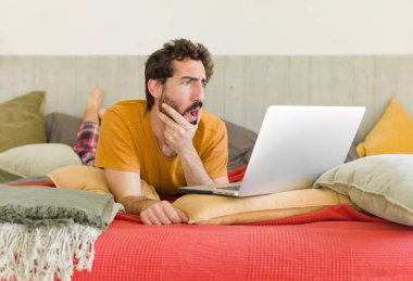 Yatakta dizüstü bilgisayarlı genç sakallı bir adam.