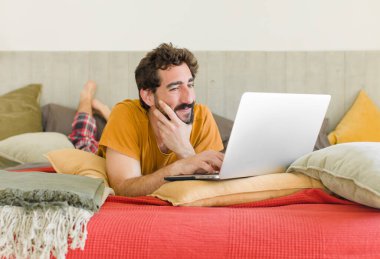 Yatakta dizüstü bilgisayarlı genç sakallı bir adam.