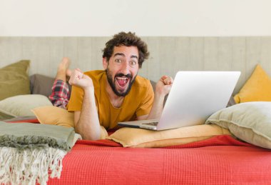 Yatakta dizüstü bilgisayarlı genç sakallı bir adam.