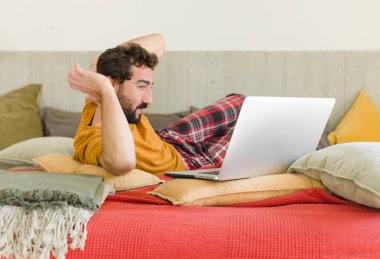 Yatakta dizüstü bilgisayarlı genç sakallı bir adam.