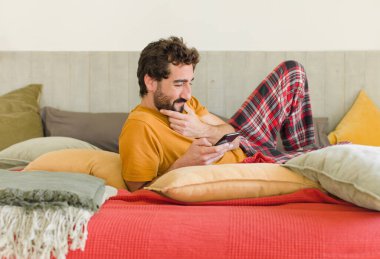 Yatakta cep telefonuyla sakallı genç bir adam.