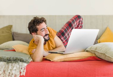 Yatakta dizüstü bilgisayarlı genç sakallı bir adam.