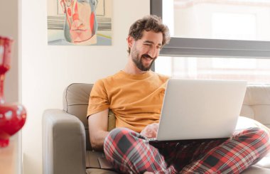 Kanepede dizüstü bilgisayarlı genç sakallı bir adam.