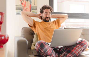 Kanepede dizüstü bilgisayarlı genç sakallı bir adam.