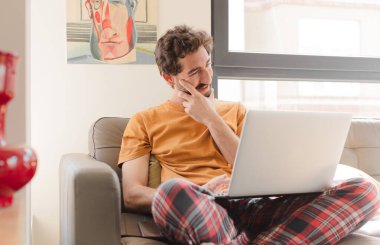 Kanepede dizüstü bilgisayarlı genç sakallı bir adam.