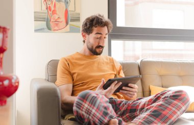 Kanepedeki sakallı genç adam Dokunmatik ekranlı tabletle