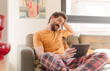 Kanepedeki sakallı genç adam Dokunmatik ekranlı tabletle