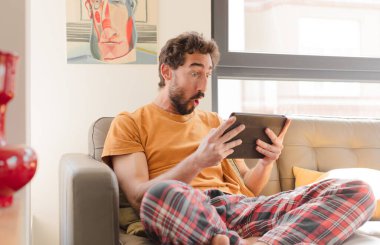 Kanepedeki sakallı genç adam Dokunmatik ekranlı tabletle