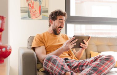 Kanepedeki sakallı genç adam Dokunmatik ekranlı tabletle