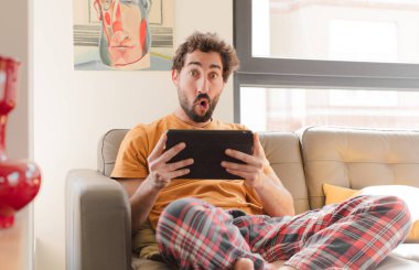 Kanepedeki sakallı genç adam Dokunmatik ekranlı tabletle