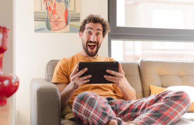 Kanepedeki sakallı genç adam Dokunmatik ekranlı tabletle