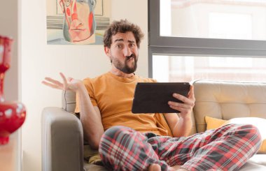 Kanepedeki sakallı genç adam Dokunmatik ekranlı tabletle