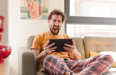 Kanepedeki sakallı genç adam Dokunmatik ekranlı tabletle