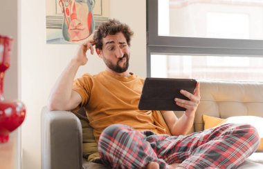 Kanepedeki sakallı genç adam Dokunmatik ekranlı tabletle