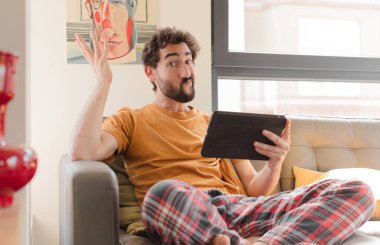 Kanepedeki sakallı genç adam Dokunmatik ekranlı tabletle