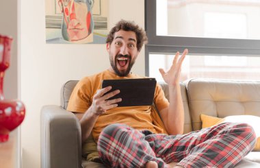 Kanepedeki sakallı genç adam Dokunmatik ekranlı tabletle