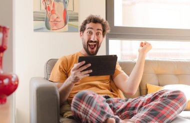 Kanepedeki sakallı genç adam Dokunmatik ekranlı tabletle