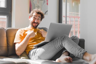 Genç sakallı adam mutlu, şaşırmış ve gururlu hissediyor. Dizüstü bilgisayarında dizüstü bilgisayarı olan heyecanlı, şaşkın bakışlarıyla kendini işaret ediyor.