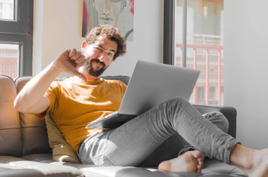 Genç sakallı adam sinirli, sinirli, hayal kırıklığına uğramış ya da hayal kırıklığına uğramış hissediyor. Dizüstü bilgisayar konseptinde dizüstü bilgisayarla ciddi bir bakış atıyor.