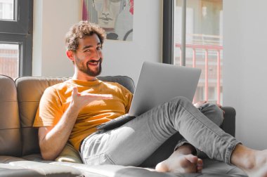 Genç sakallı adam mutlu bir şekilde gülümsüyor, kendini mutlu hissediyor ve dizüstü bilgisayarında bir dizüstü bilgisayarla fotokopi odasında bir konsept gösteriyor.