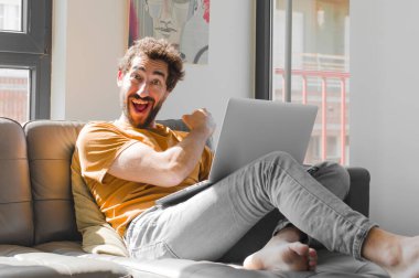 Genç sakallı adam mutlu, pozitif ve başarılı hissediyor. Zorlukla karşılaştığında ya da dizüstü bilgisayarla iyi sonuçlar aldığında motive oluyor.