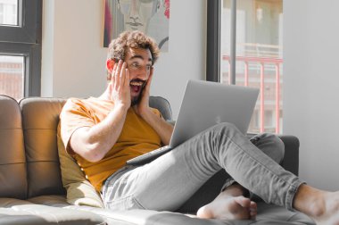 Genç sakallı adam mutlu, heyecanlı ve şaşırmış hissediyor. Dizüstü bilgisayarında dizüstü bilgisayarı olan iki eliyle yan tarafa bakıyor.