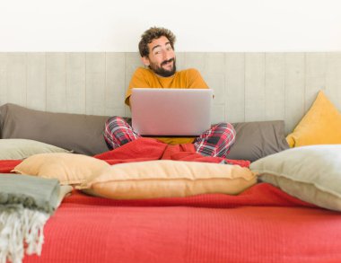 Genç sakallı adam omuz silkiyor, kafası karışık ve emin değil, kolları bağlı ve şaşkın görünüyor.